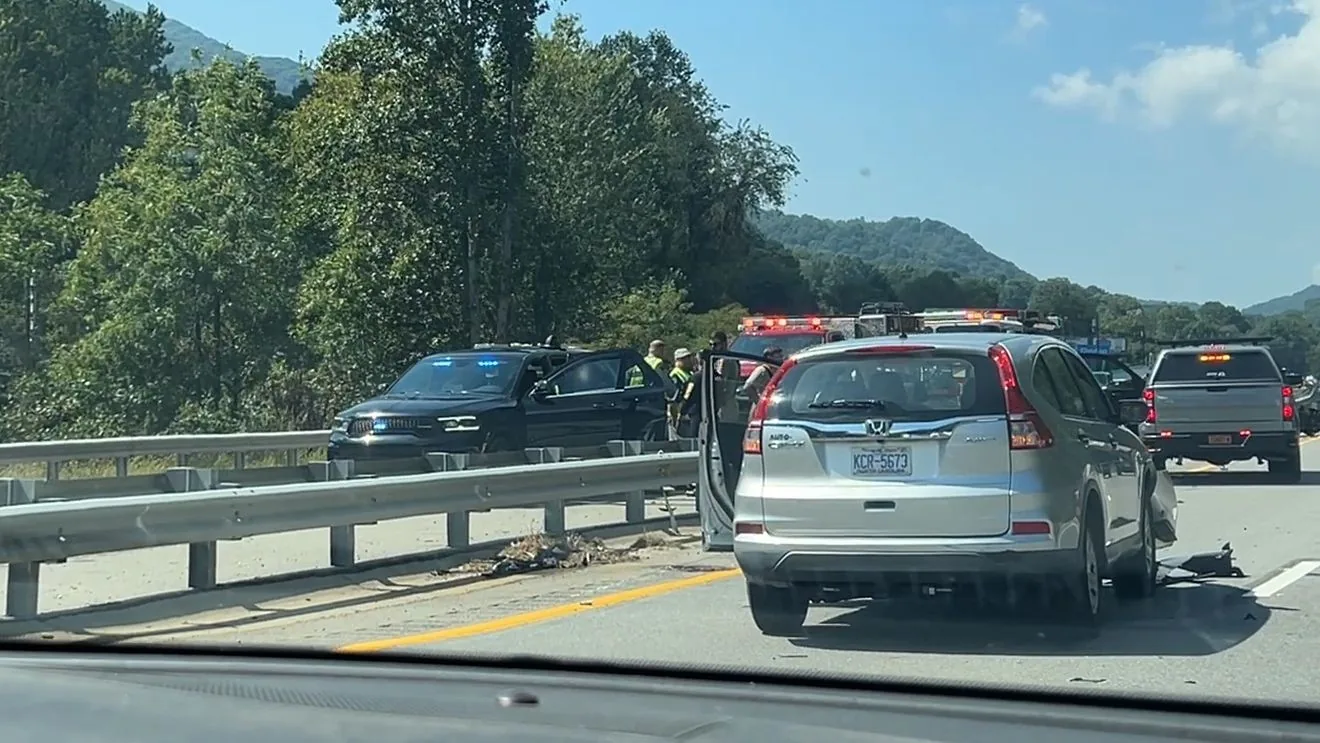 Police investigate a motorcycle crash scene on a highway with a guardrail and stopped vehicles